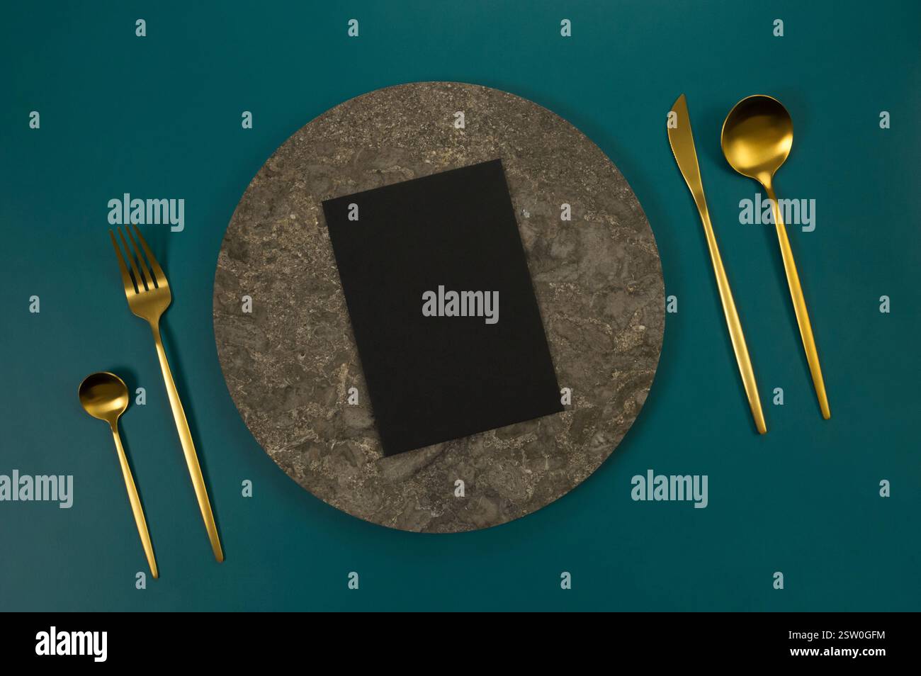 Blick von oben auf braunen Marmorteller, goldenes Besteck und schwarze Karte auf dunkelgrünem Hintergrund. Essenspräsentation, Steintablett. Tabelleneinstellung, Kopierbereich. Stockfoto