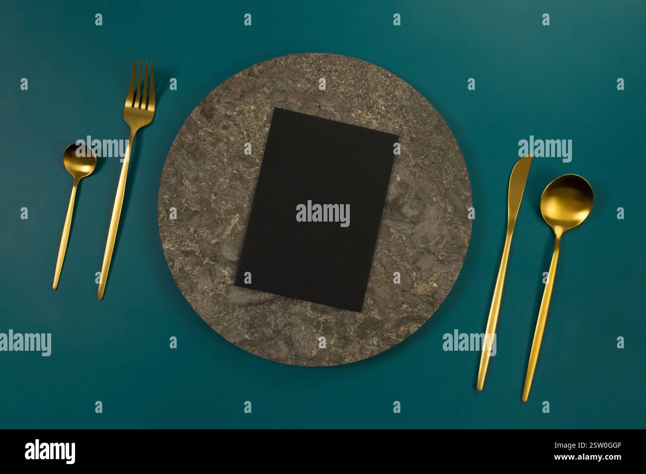 Blick von oben auf braunen Marmorteller, goldenes Besteck und schwarze Karte auf dunkelgrünem Hintergrund. Essenspräsentation, Steintablett. Tabelleneinstellung, Kopierbereich. Stockfoto