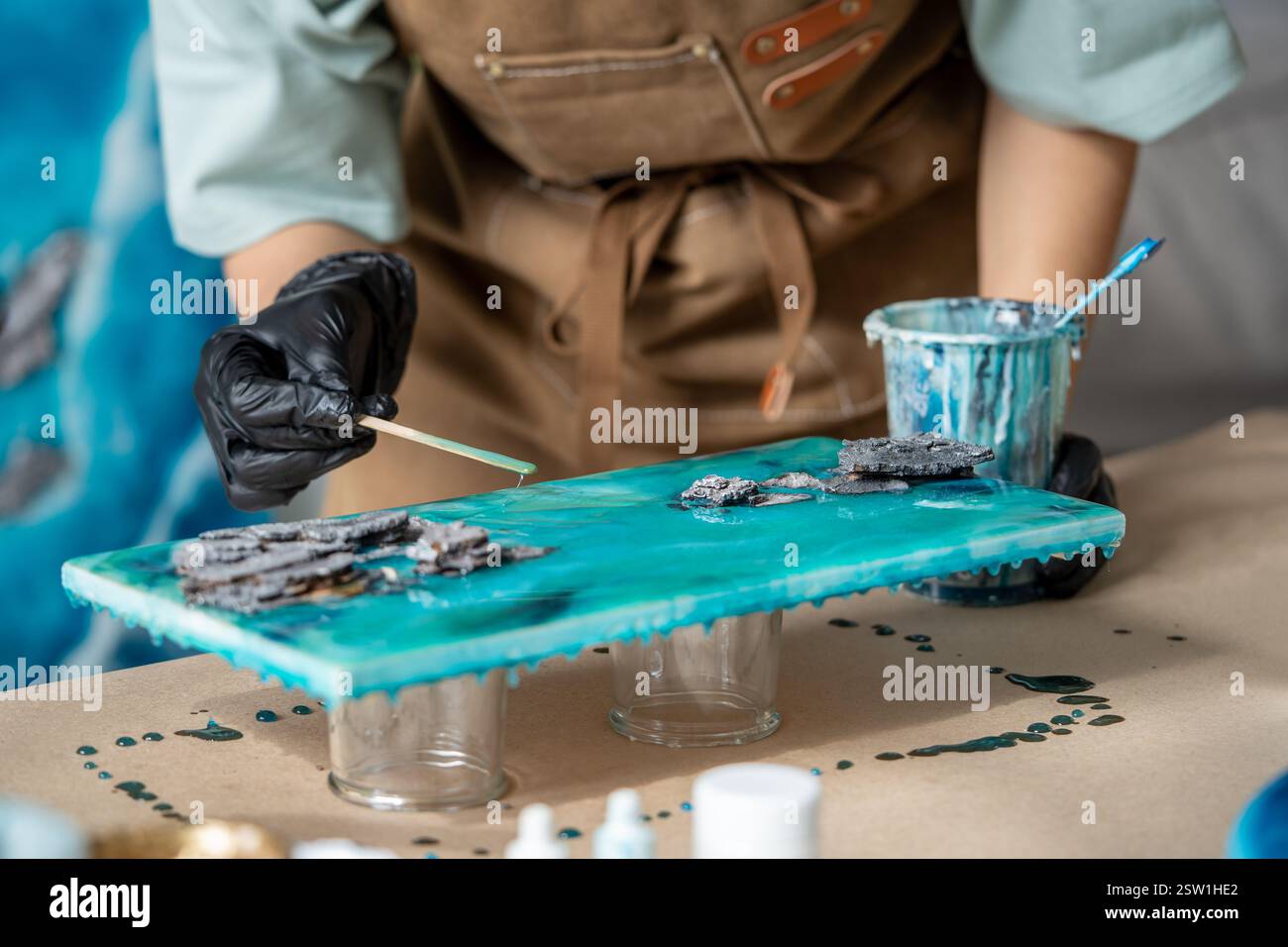 Die Künstlerin gießt Epoxidharz und schmiert es mit einem Stock auf Holzbrett, mit Hilfe von Flüssigkunsttechnik Stockfoto