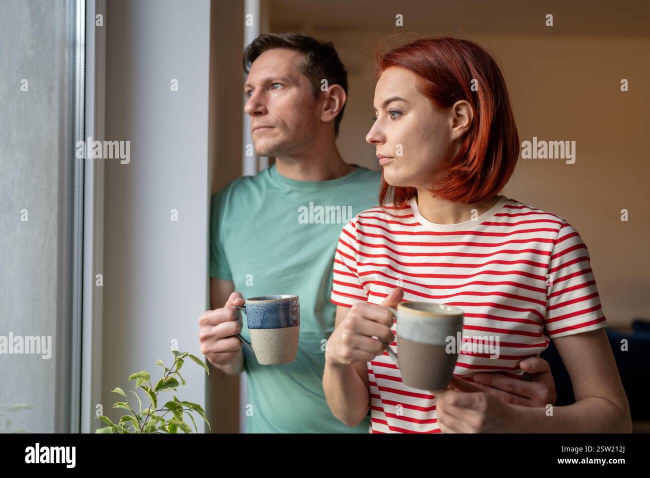 Aufgewühltes Mädchen und Mann halten eine Tasse Kaffee, schauen aus dem Fenster, fühlen sich traurig und ängstlich. Familienprobleme Stockfoto