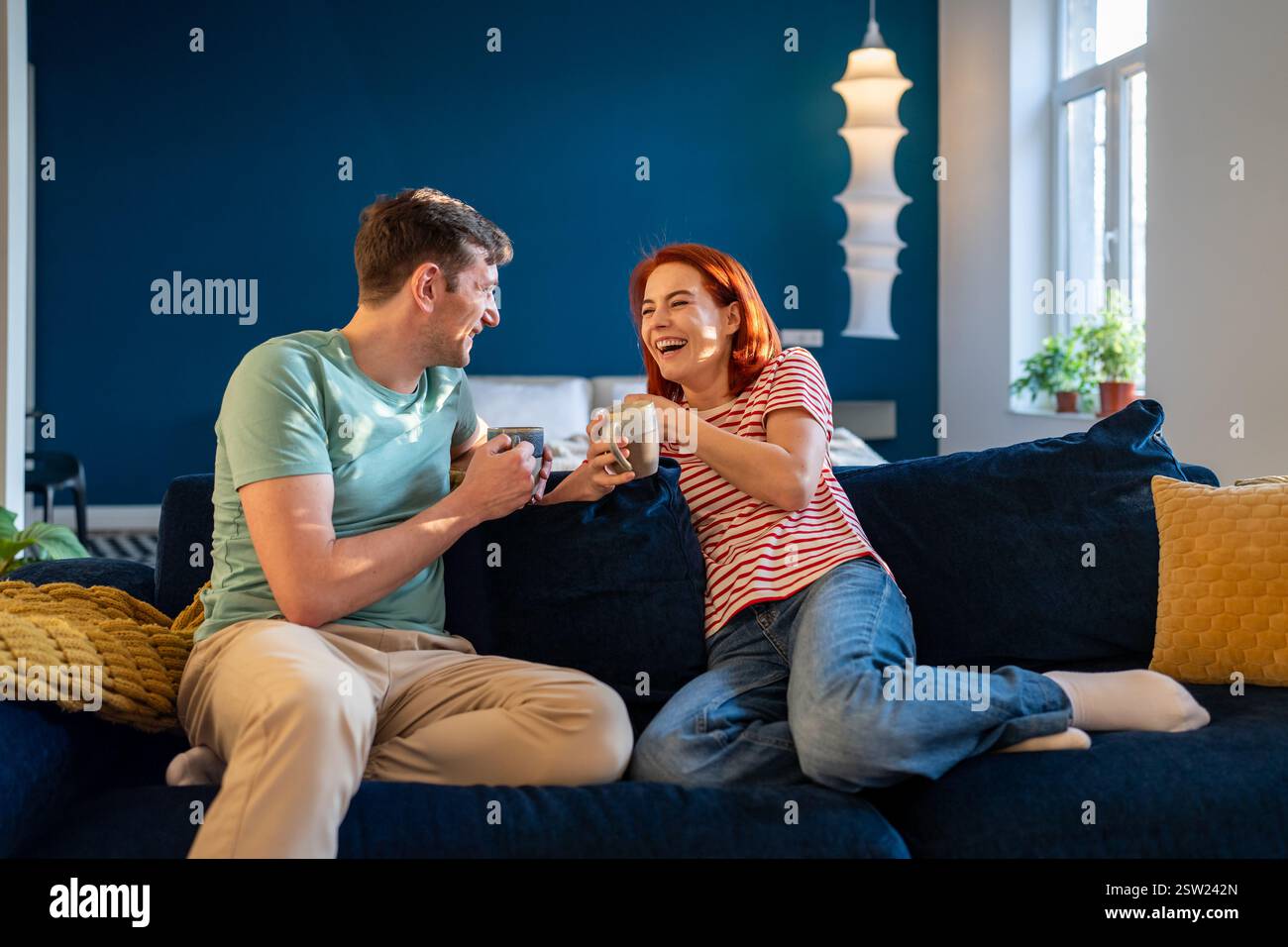 Glückliches junges Paar, das sich entspannt und sich mit Kaffee auf der Couch unterhält. Emotionale Verbindung in der Beziehung Stockfoto