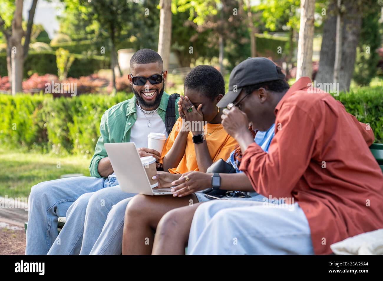 Fröhliche, überfröhliche Gruppe afroamerikanischer Freunde, die mit einem Laptop sitzen und lachen und gemeinsam Spaß haben. Stockfoto