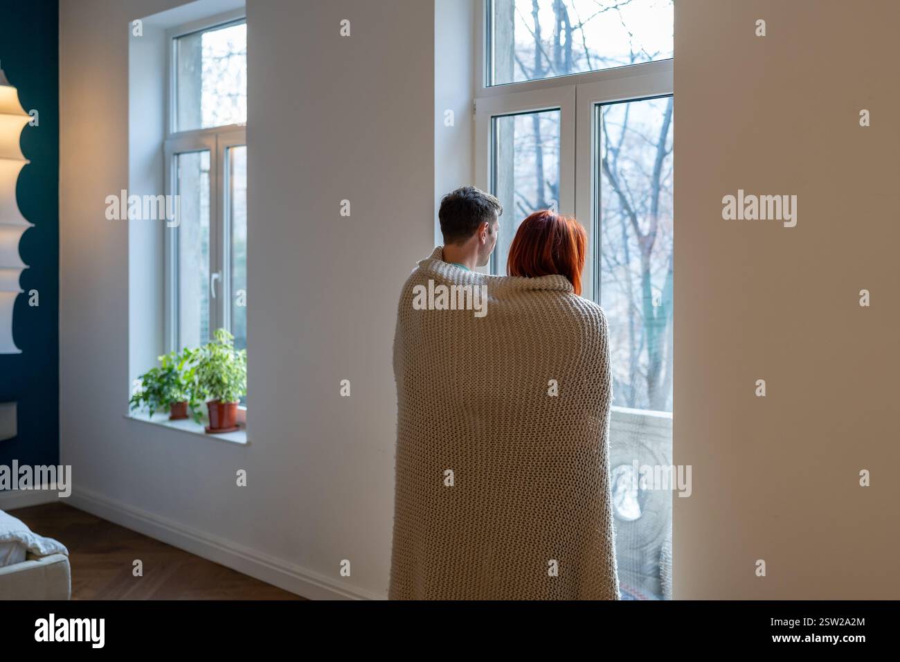 Ein Paar, in eine Decke gewickelt, mit Blick aus dem Fenster Stockfoto