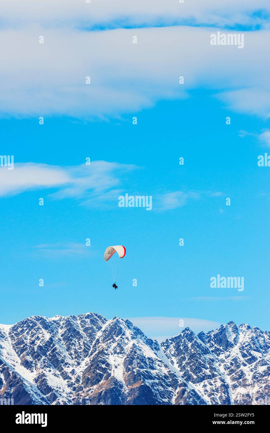 Gleitschirmfliegen über die schneebedeckten Remarkables Bergketten in Queenstown, Südinsel, Neuseeland Stockfoto