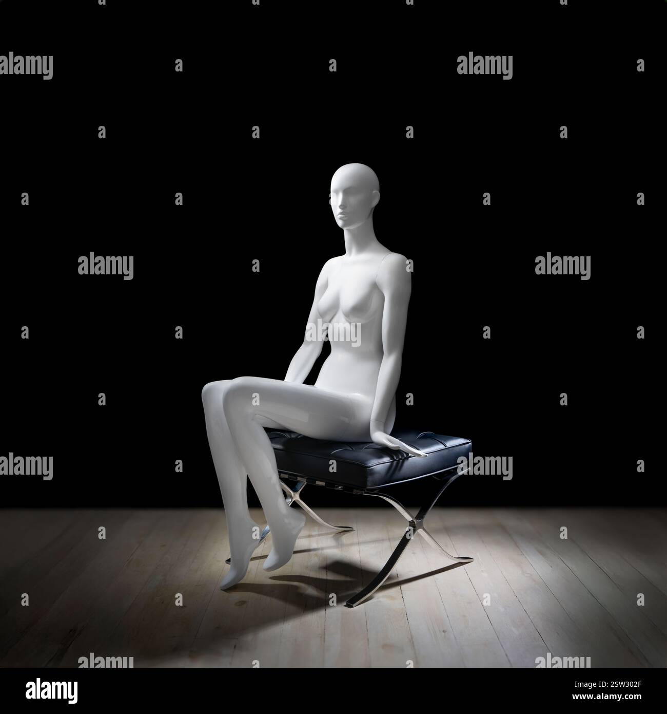 Eine weiße Schaufensterpuppe auf Ledersitz im Barcelona-Stil, umgeben von einem minimalistischen dunklen Studio. Stockfoto