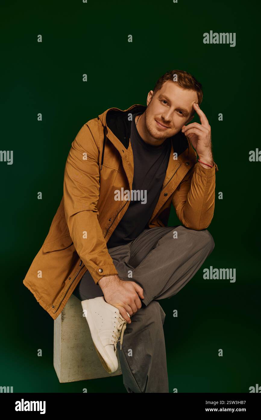 Ein gutaussehender Mann in lässigem Outfit sitzt nachdenklich auf einem Block und hebt moderne Mode hervor. Stockfoto