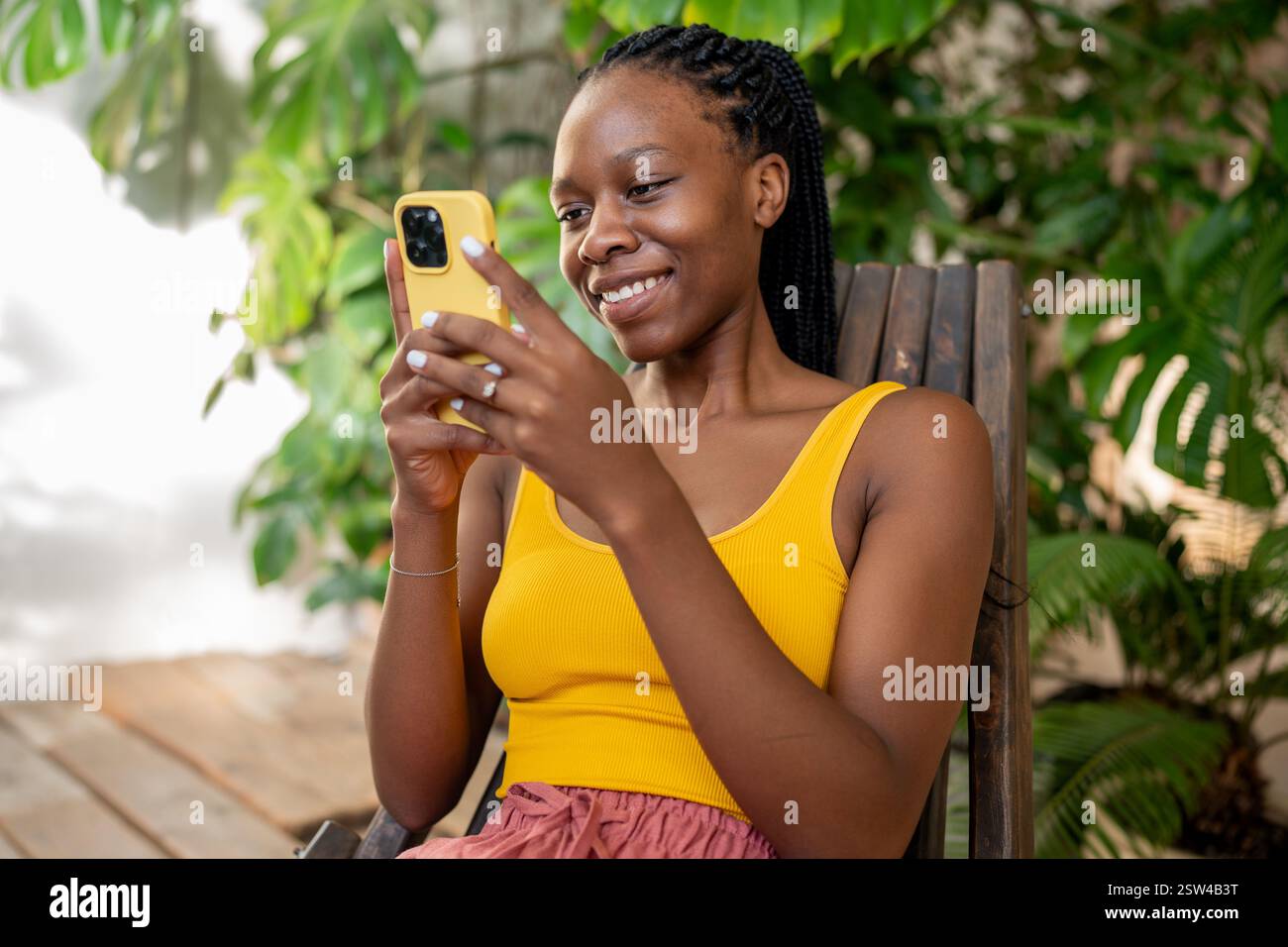 Kichernde Afroamerikanerin mit Telefon. Glückliches Mädchen, das sich im urbanen Dschungel zu Hause entspannt. Stockfoto