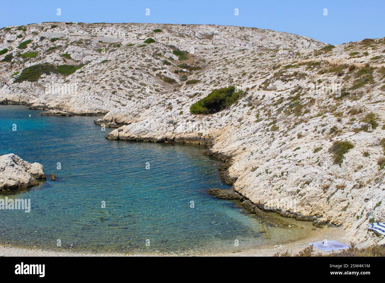 Malerische mediterrane Bucht mit Segelboot – Frankreich. Ein atemberaubender Blick auf eine mediterrane Bucht mit türkisfarbenem Wasser, zerklüfteten Klippen und einem Segelboot. Stockfoto