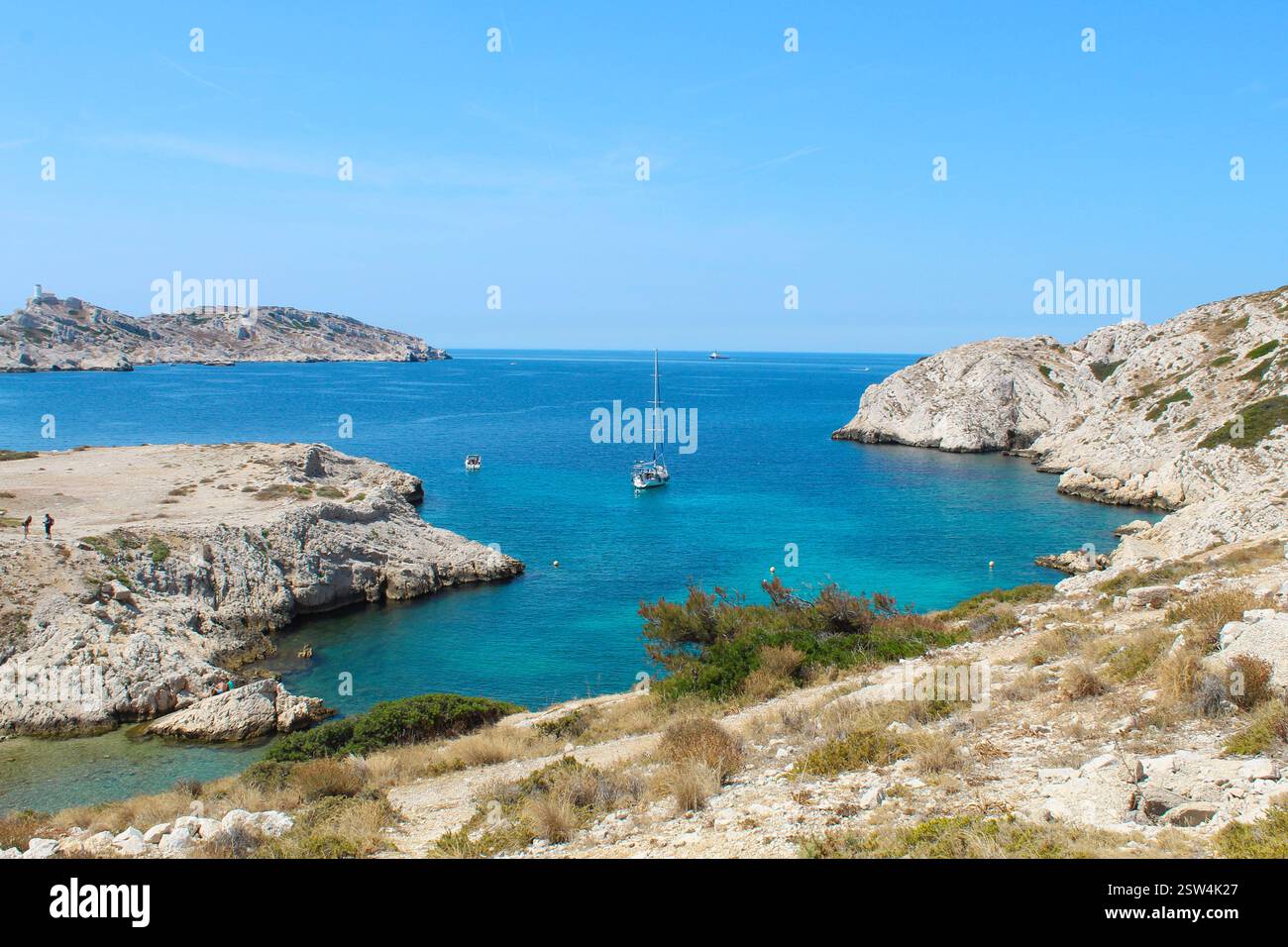 Malerische mediterrane Bucht mit Segelboot – Frankreich. Ein atemberaubender Blick auf eine mediterrane Bucht mit türkisfarbenem Wasser, zerklüfteten Klippen und einem Segelboot. Stockfoto