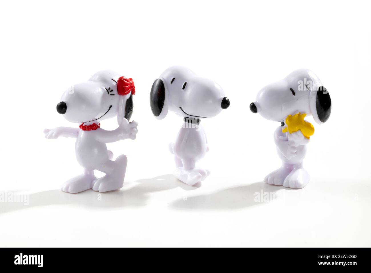 Drei Plastik-Snoopy-Figuren aus dem beliebten Peanuts-Comic stehen auf weißem Hintergrund, jede mit einem anderen Ausdruck Stockfoto