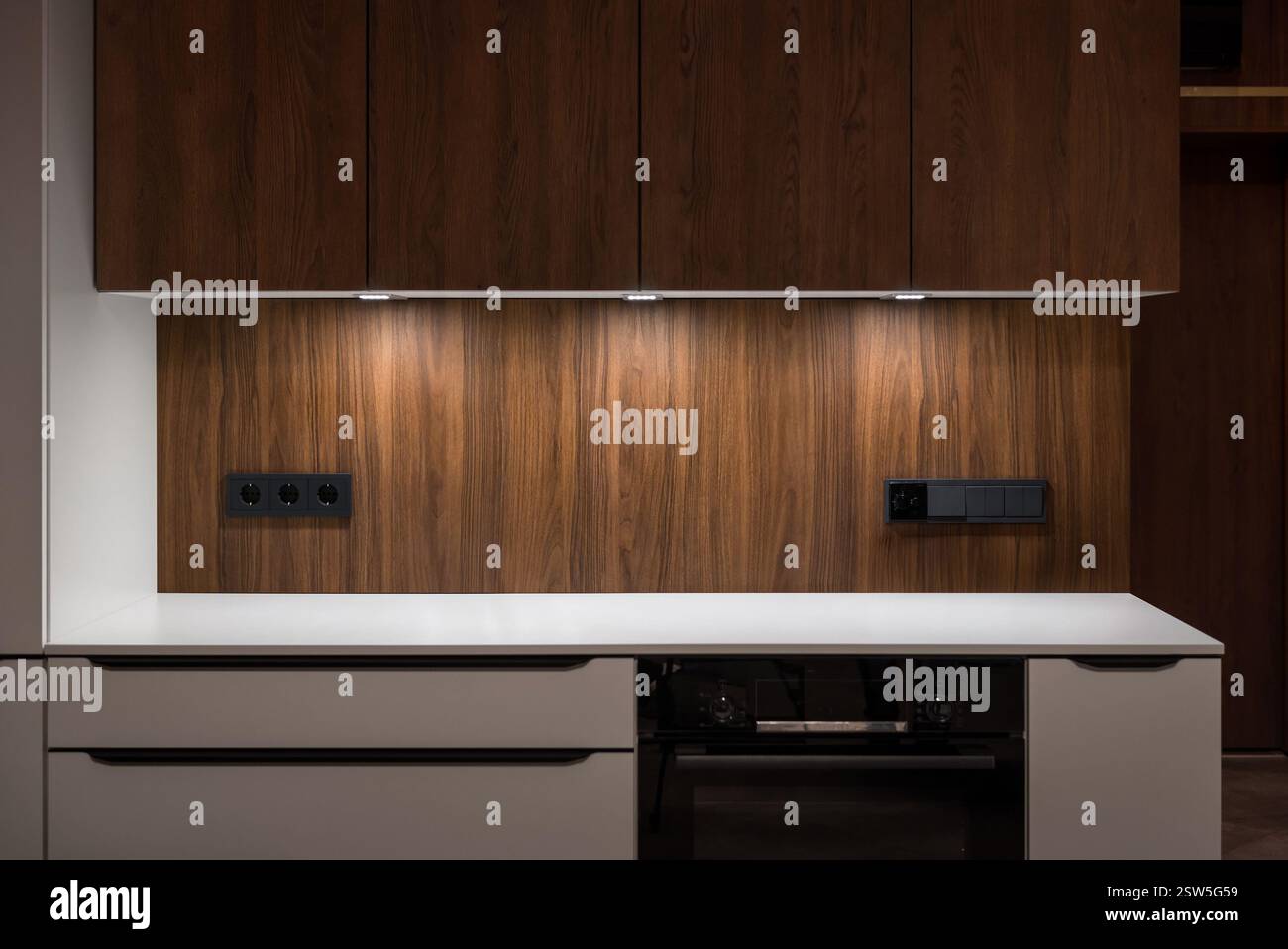 Moderne braune Kücheneinrichtung. Helle leere beleuchtete Arbeitsplatte – flache Perspektive Stockfoto