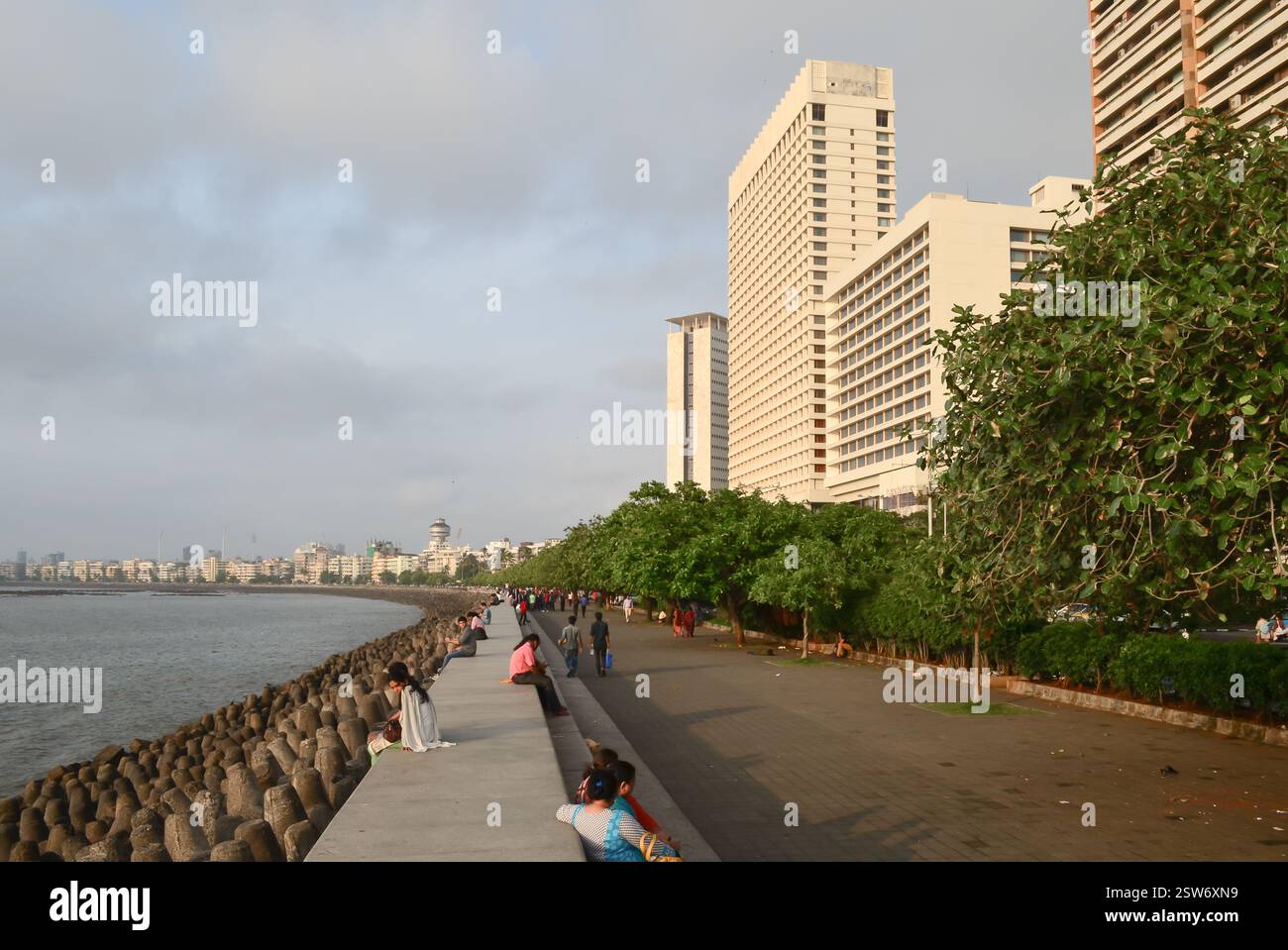 Menschen sitzen entlang der Marine Drive Promenade in der Nähe von Nariman Point mit Hotel-Hochhäusern und Wellenbrecher-Tetrapoden in Süd-Mumbai. Stockfoto