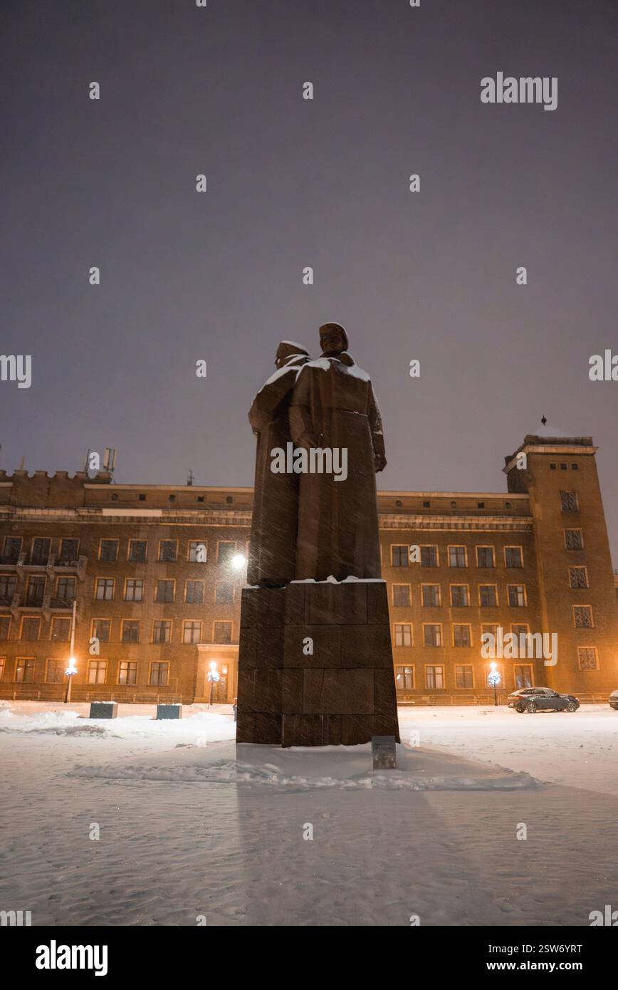 Schneebedecktes Denkmal und beleuchtetes Gebäude auf dem Rigaer Platz Stockfoto