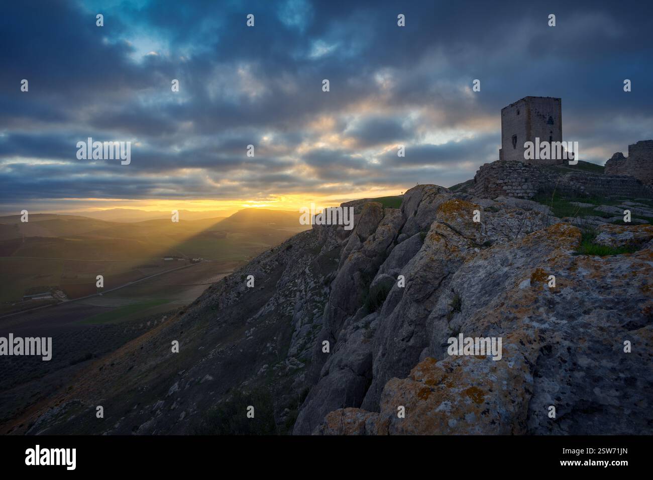 Sonnenuntergang im Schloss von La Estrella, Teba. Der antike Turm auf dem felsigen Gipfel, der dramatische Himmel und das goldene Licht über Andalusien Stockfoto