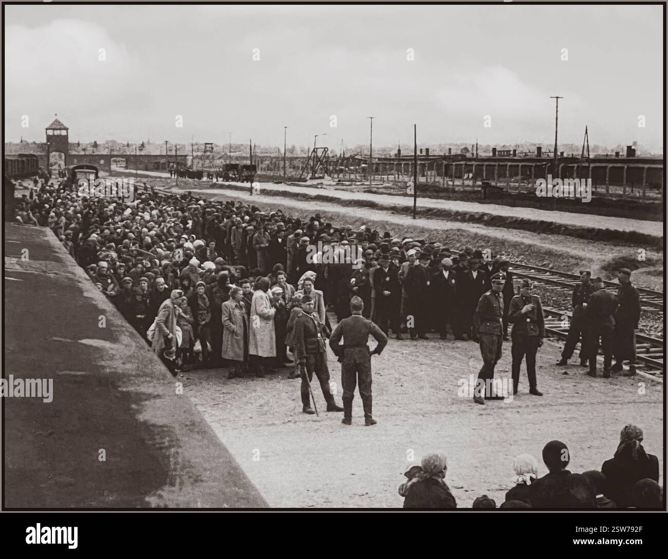 AUSCHWITZ-BIRKENAU-HOLOCAUST-GEFANGENE BAHNANKOMMEN--Eine Vision der Hölle auf Erden. 1944. Nazis-Truppen in Militäruniform, die Jackstiefel tragen, "Grading" (Leben oder Tod) ahnungslose männliche und weibliche Gefangene auf der Bahnhalle vor dem Eingang zum Vernichtungslager Auschwitz-Birkenau. Das berüchtigte Lager Auschwitz wurde 1940 auf Befehl Adolf Hitlers während der Besetzung Polens durch Nazi-Deutschland im Zweiten Weltkrieg gegründet. Er wurde von Heinrich Luitpold Himmler, dem Reichsführer der Schutzstaffel und führenden Mitglied der NSDAP Deutschlands, begeistert ermöglicht. Stockfoto