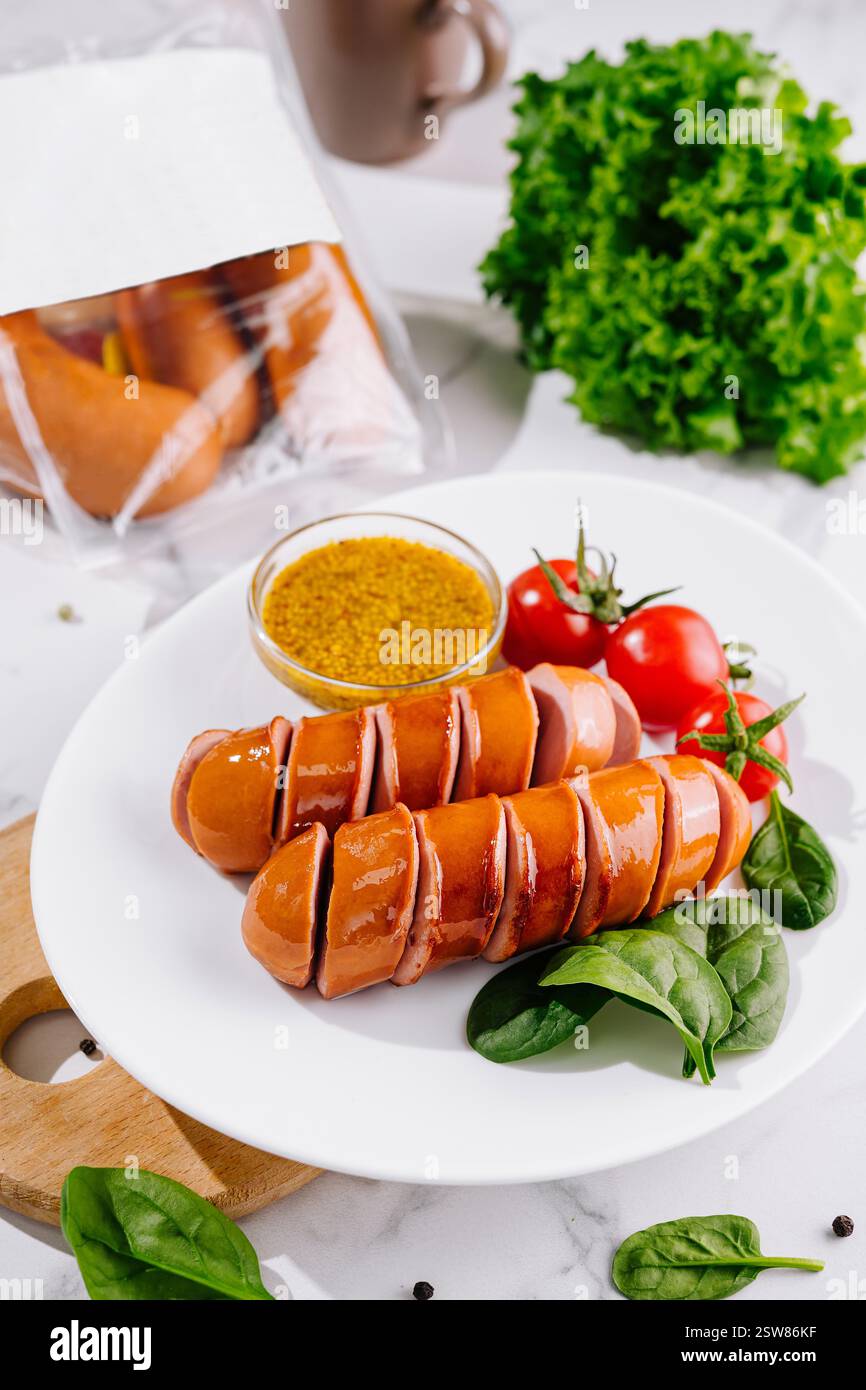 Würstchen in Scheiben auf weißem Teller mit Senfgrün und Tomaten Stockfoto