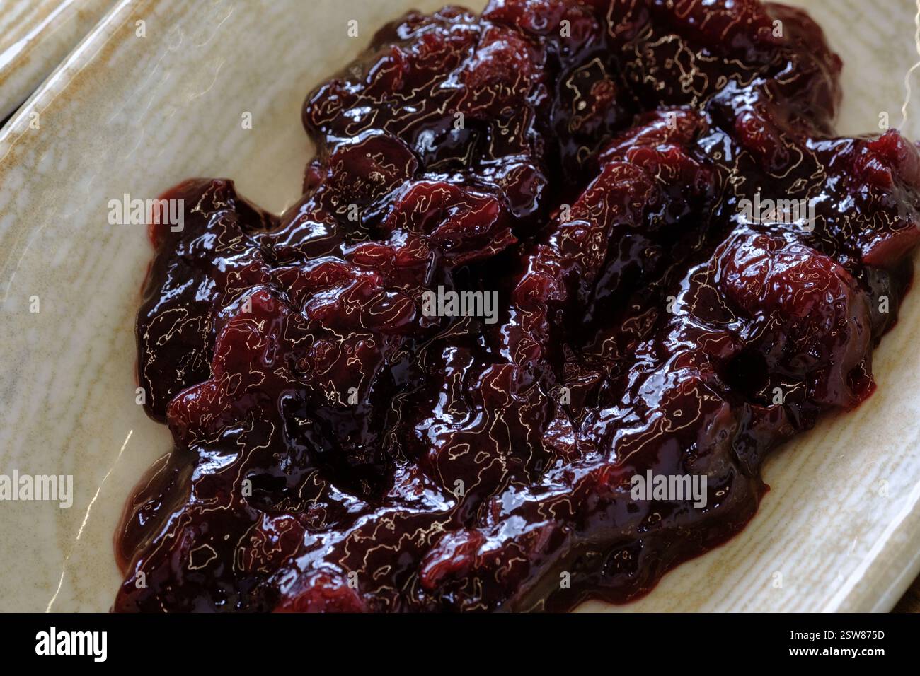 Eine Nahaufnahme dunkler, glänzender Fruchtkonserven, möglicherweise Kirsch oder Pflaume in einem flachen Gericht reichhaltig und dekadent Stockfoto