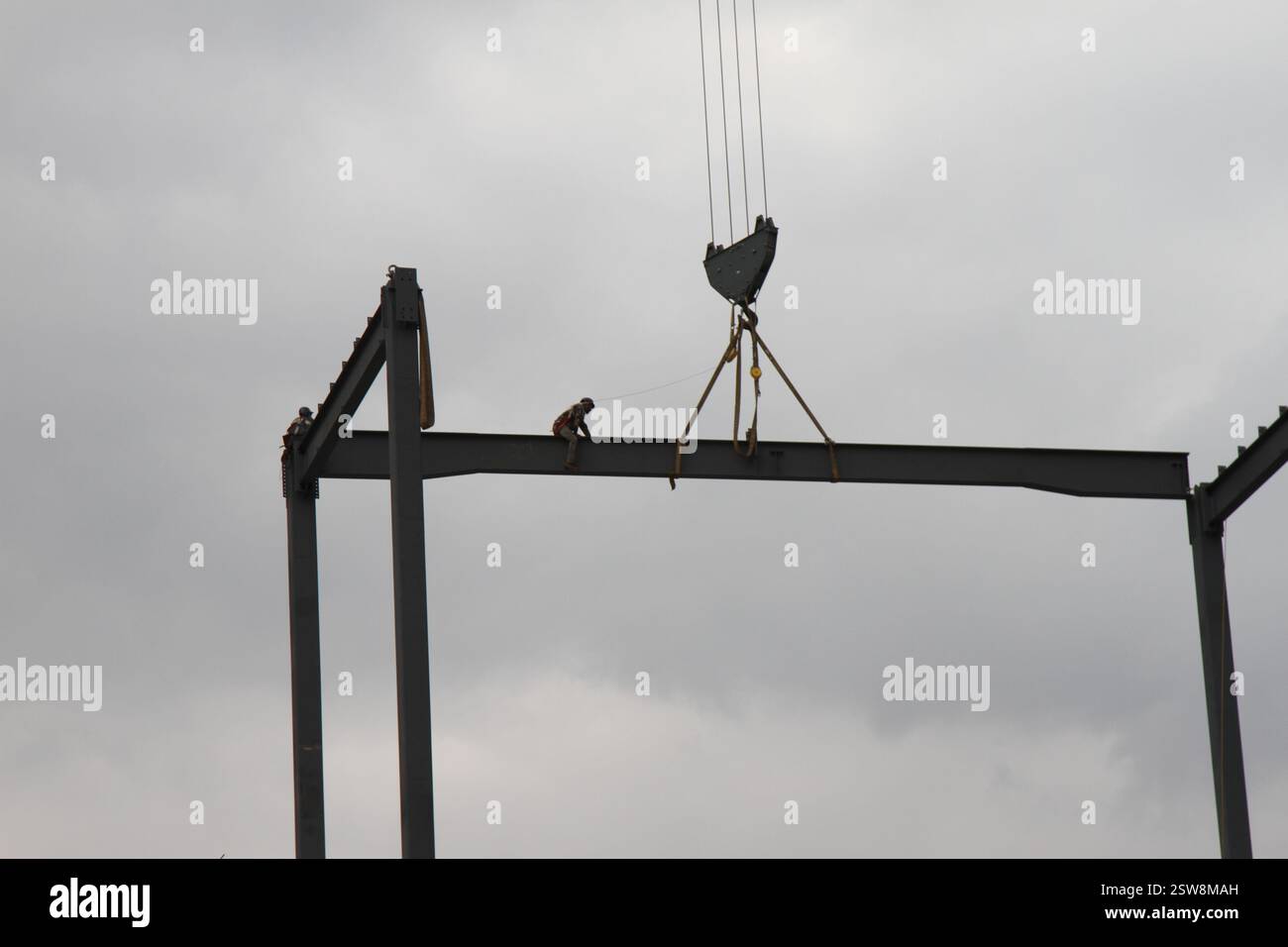 Ein Bauarbeiter auf einem Stahlträger in der Höhe, während er mit einem Baukran transportiert wird. Ein Mann, der im Bau arbeitet. Stockfoto