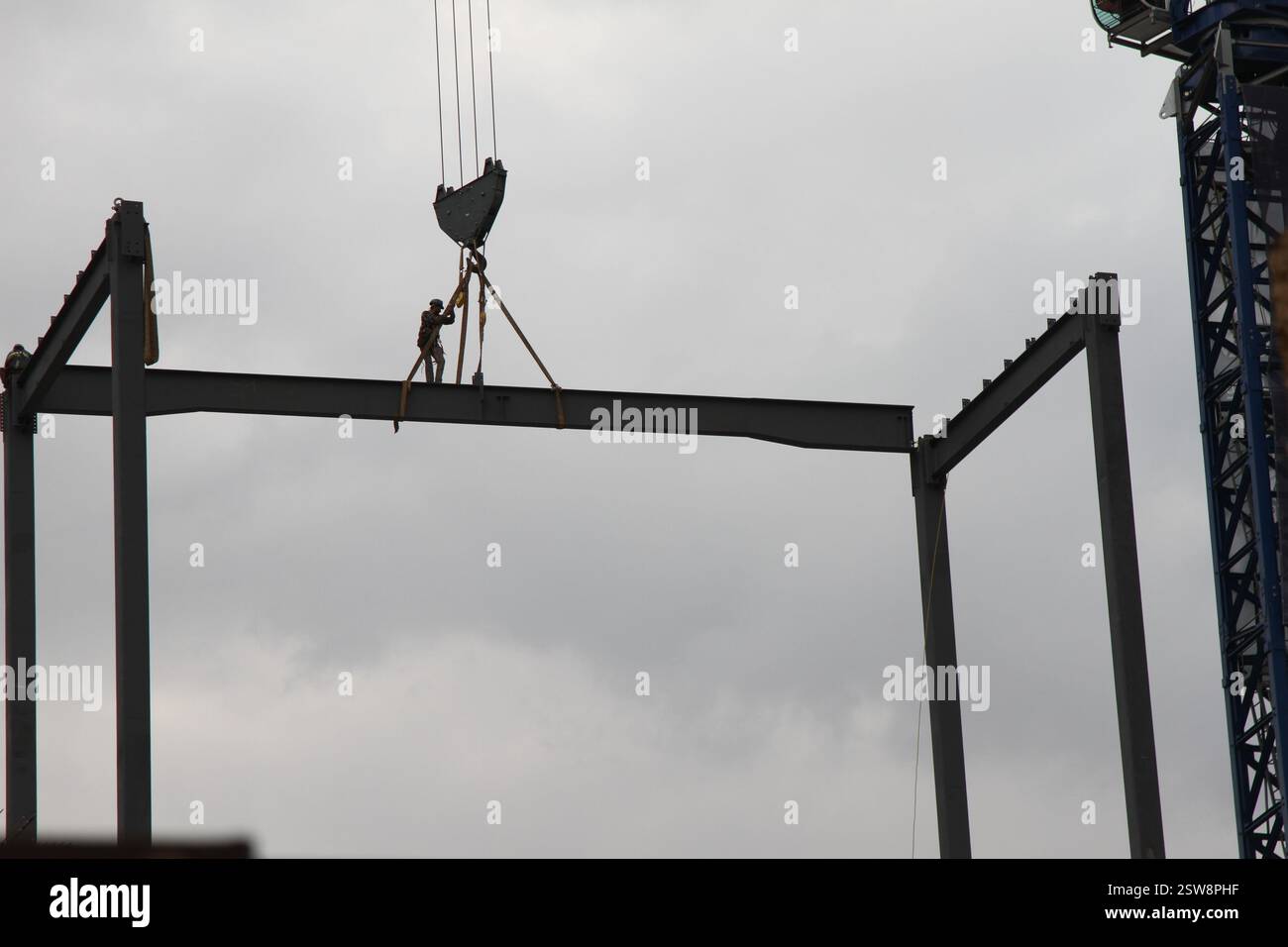 Ein Bauarbeiter auf einem Stahlträger in der Höhe, während er mit einem Baukran transportiert wird. Ein Mann, der im Bau arbeitet. Stockfoto