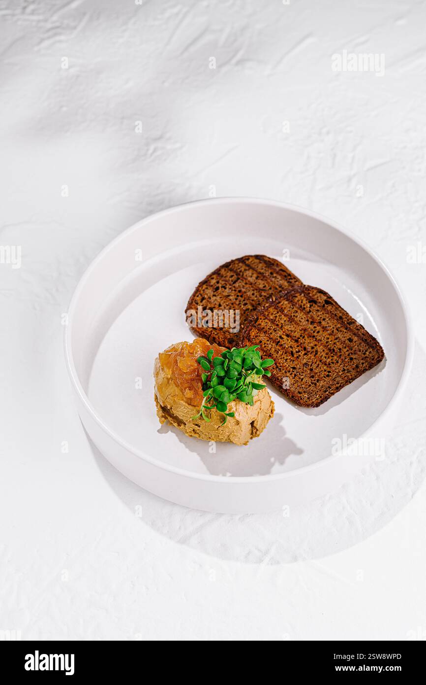Hühnerleberpastete mit Mangopüree und Roggenbrot auf weißem Teller Stockfoto