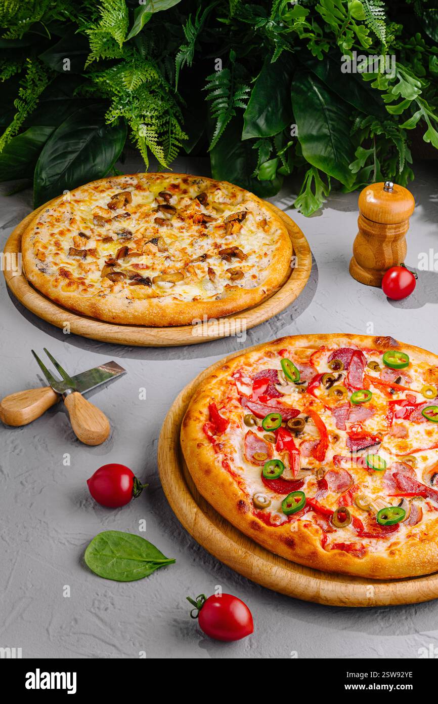 Zwei köstliche Pizzen auf Holztabletts, umgeben von frischen Zutaten Stockfoto