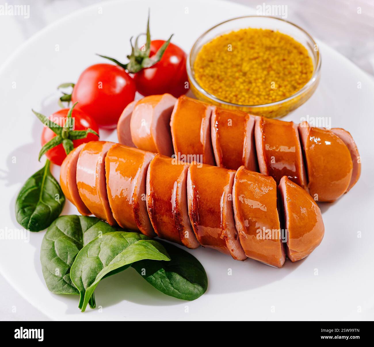 Würstchen in Scheiben auf weißem Teller mit Senfgrün und Tomaten Stockfoto