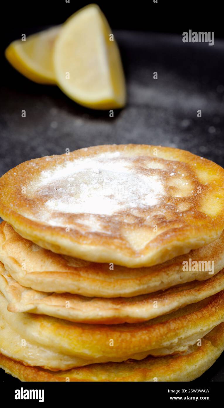 Ein Stapel Pfannkuchen mit Puderzucker drauf. Die Pfannkuchen werden übereinander gestapelt, und ein Zitronenkeil wird auf den Stapel gelegt Stockfoto