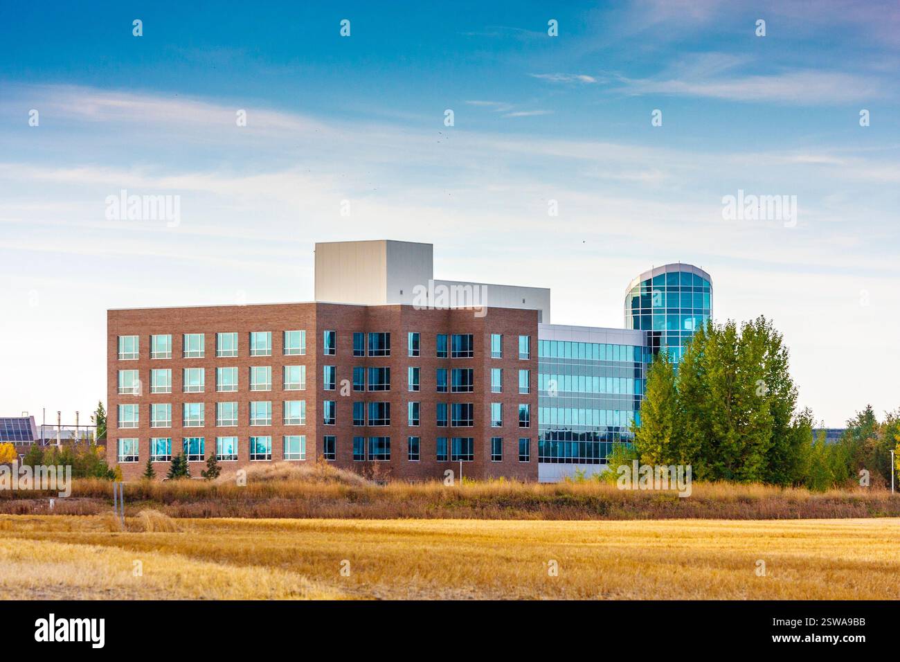 Ein großes Backsteingebäude mit einer Glasfassade befindet sich auf einem Feld. Der Himmel ist klar und die Sonne scheint Stockfoto
