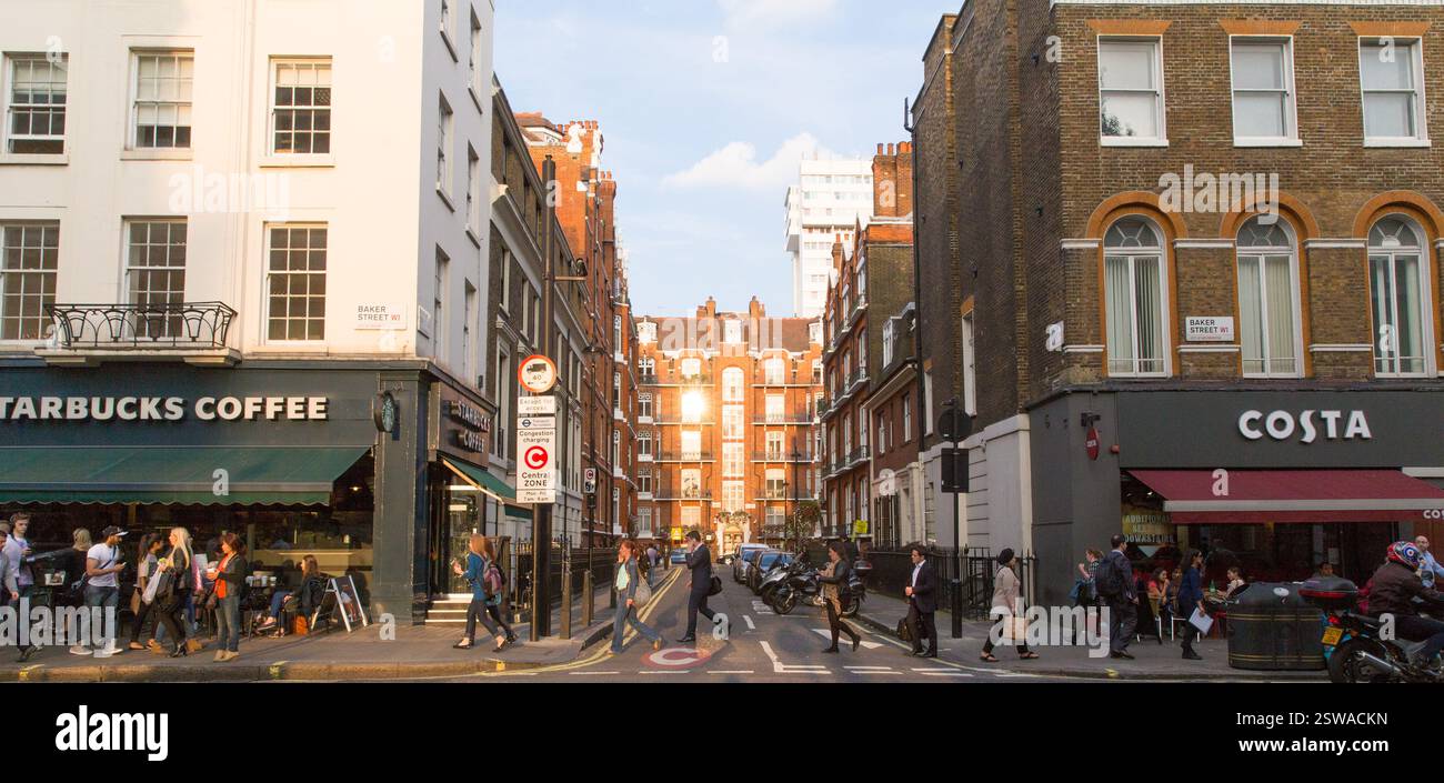 Fußgänger überqueren die Baker Street, London, in der Nähe von Starbucks und Costa Coffee Shops. Sonnenlicht hebt die roten Backsteingebäude hervor. Stockfoto