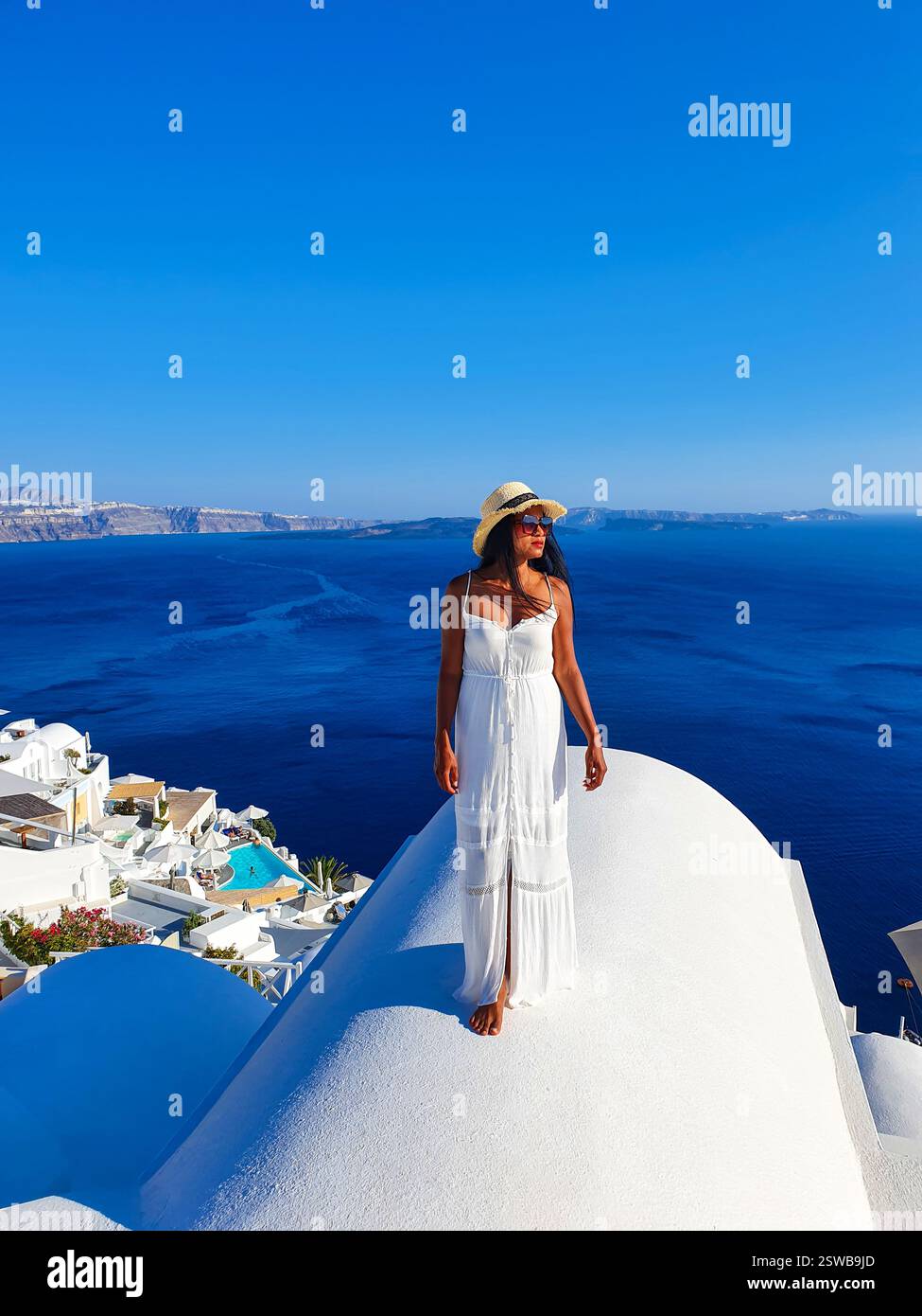 Eine Frau in einem weißen Kleid genießt die atemberaubende Aussicht auf Santorin unter dem hellblauen Himmel Stockfoto