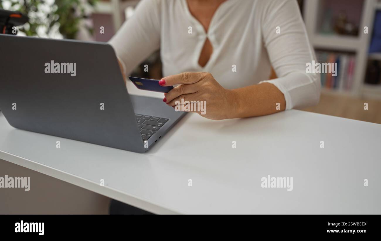 Frau, die zu Hause online mit Laptop und Kreditkarte einkaufen möchte, zeigt Hände mittleren Alters und Erwachsene in Inneneinrichtung Stockfoto