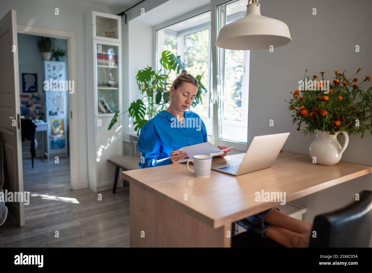Konzentrierte Frau arbeitet am Laptop, schreibt Notizen in das Notebook und organisiert den Zeitplan für Aufgaben im Home Office Stockfoto