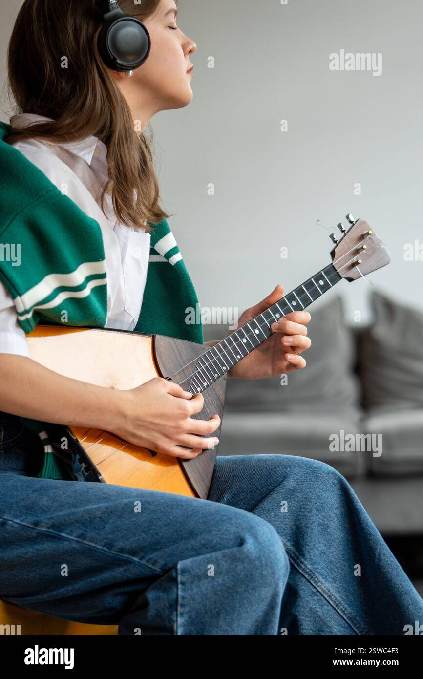Frau genießt Musik, spielt Balalaika, hört Songs über Kopfhörer zu Hause. Gehörtraining Stockfoto