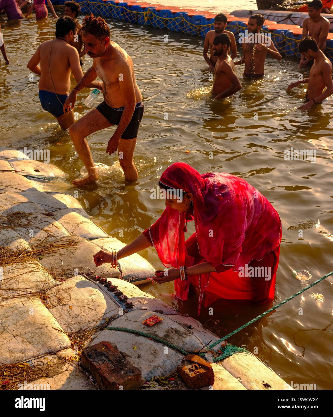 Während der Maha Kumbh Mela in Prayagraj spielt eine Frau im roten Sari Puja im Triveni Sangam, dem heiligen Zusammenfluss von Ganges, Yamuna und Saraswati. Stockfoto