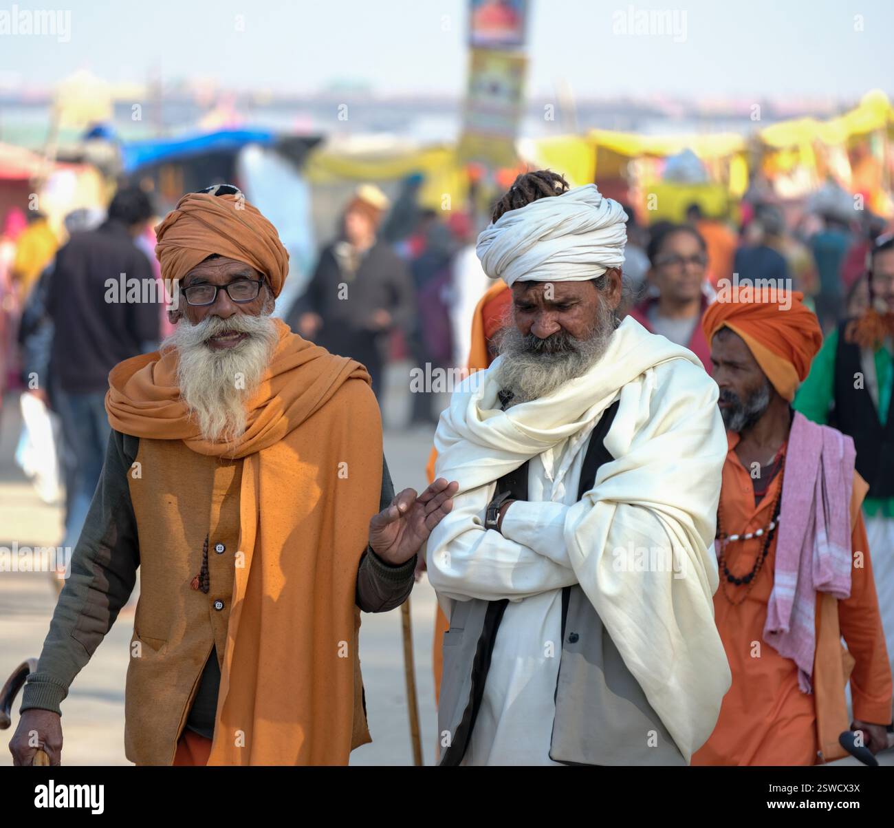 Zwei ältere Pilger in traditioneller Kleidung spazieren durch die lebhaften Massen von Maha Kumbh Mela in Prayagraj, die die Spiritualität der Feier verkörpern. Stockfoto