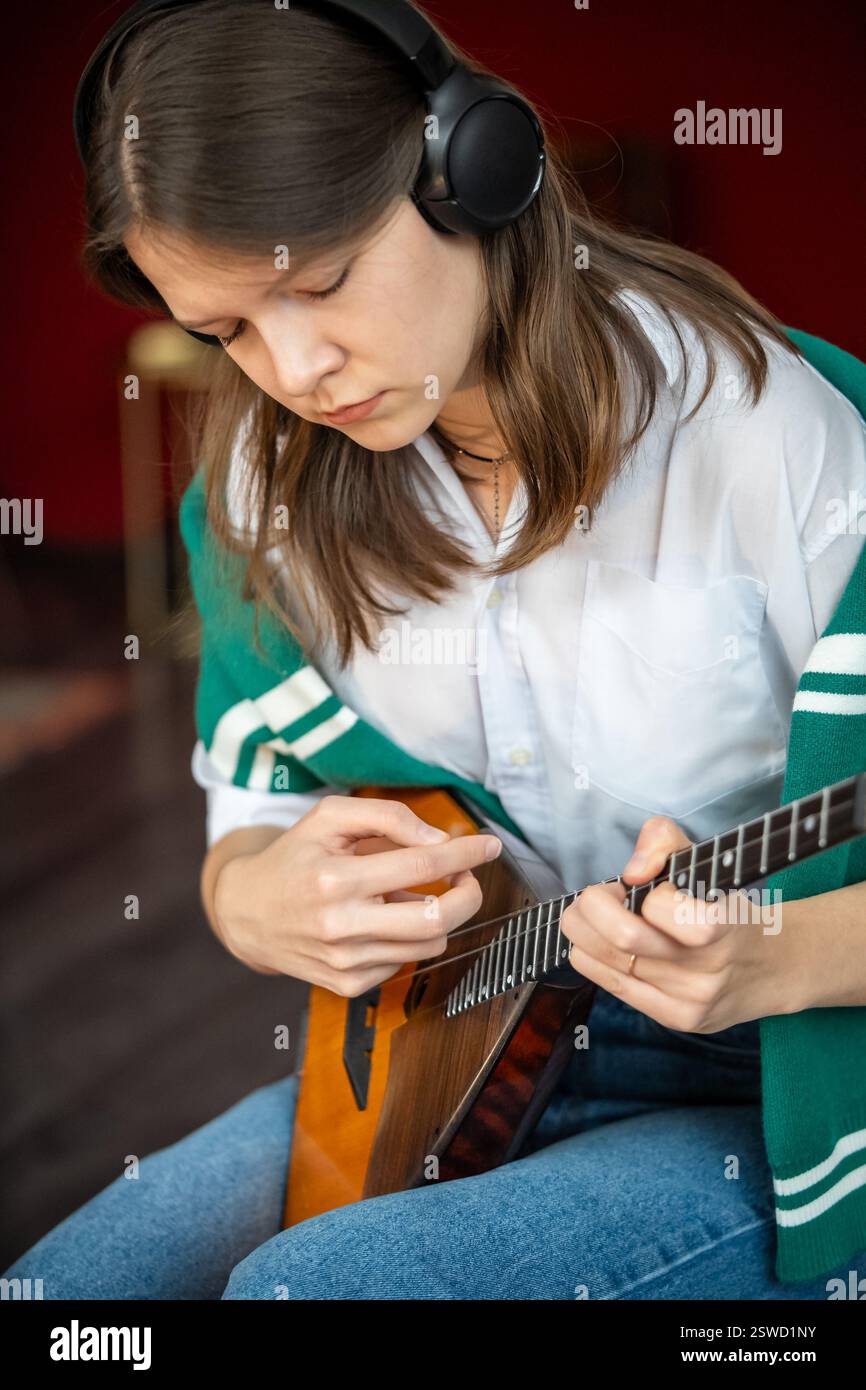 Frau übt Balalaika-Akkorde mit Kopfhörern, während sie im Rhythmus spielt. Musikübungen zu Hause Stockfoto