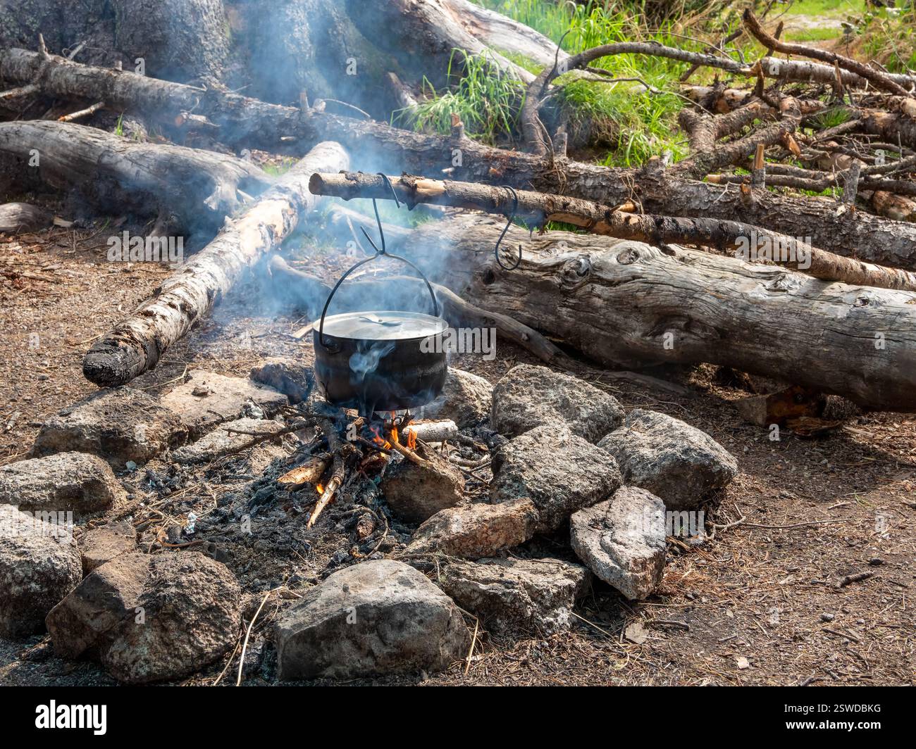 Campingküche. Kochen von Essen am Feuer in der Wildnis. Wasserkocher in Ruß, der über dem Feuer hängt. Uberleben in der wilden Natur. Wundervolle Flamme mit c Stockfoto