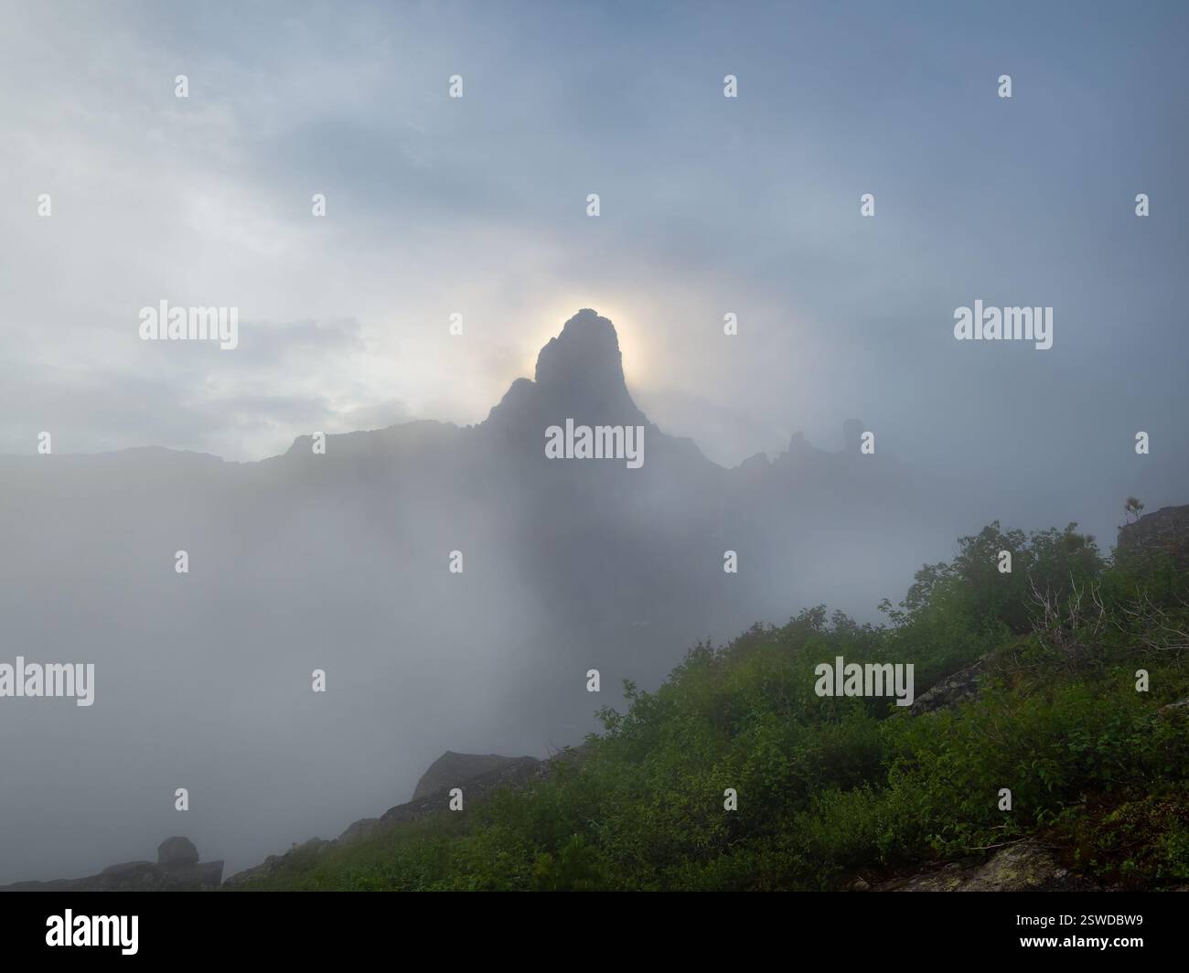 Morgensonne hinter dem Berggipfel, Sonnenaufgang in den nebeligen Bergen. Atmosphärischer geisterhafter Minimalismus mit großen Berggipfeln i Stockfoto