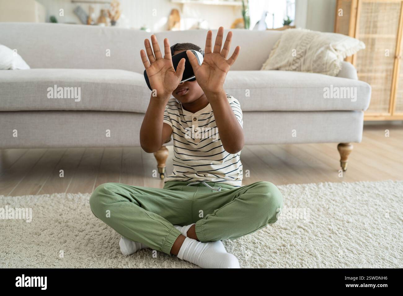 Ein kleiner, neugieriger afroamerikanischer Junge mit VR-Brille, der Zeit in der virtuellen Welt verbringt Stockfoto