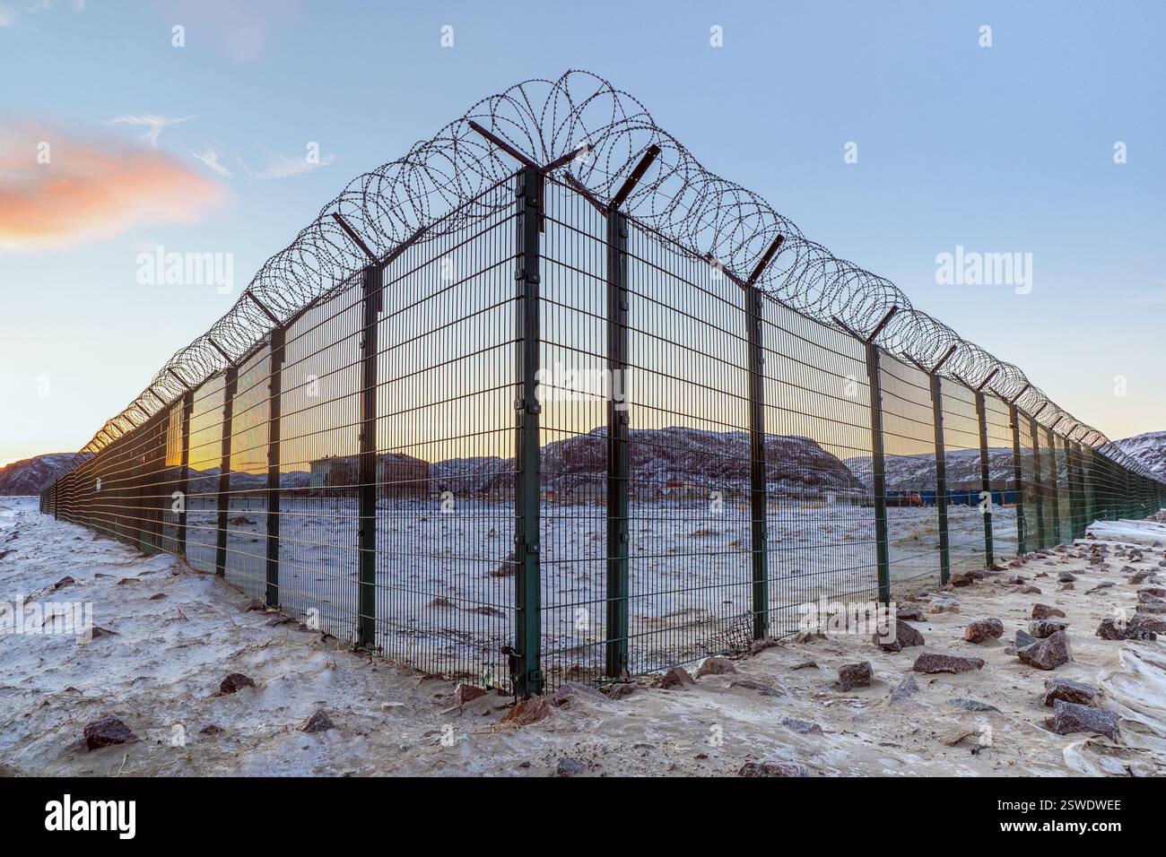 Eine Ecke eines Zauns mit Stacheldraht auf dem Hintergrund des Abendhimmels in einem arktischen Dorf. Stockfoto