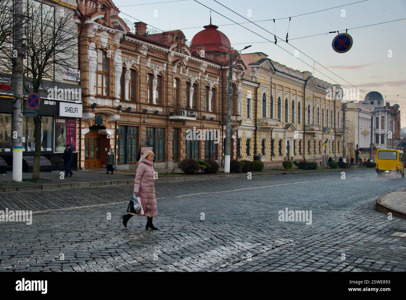 Am 20. Dezember 2023 überquert eine Frau die Straße vor einigen der historischen Gebäude in Kropyvnytskyi, Ukraine. Stockfoto