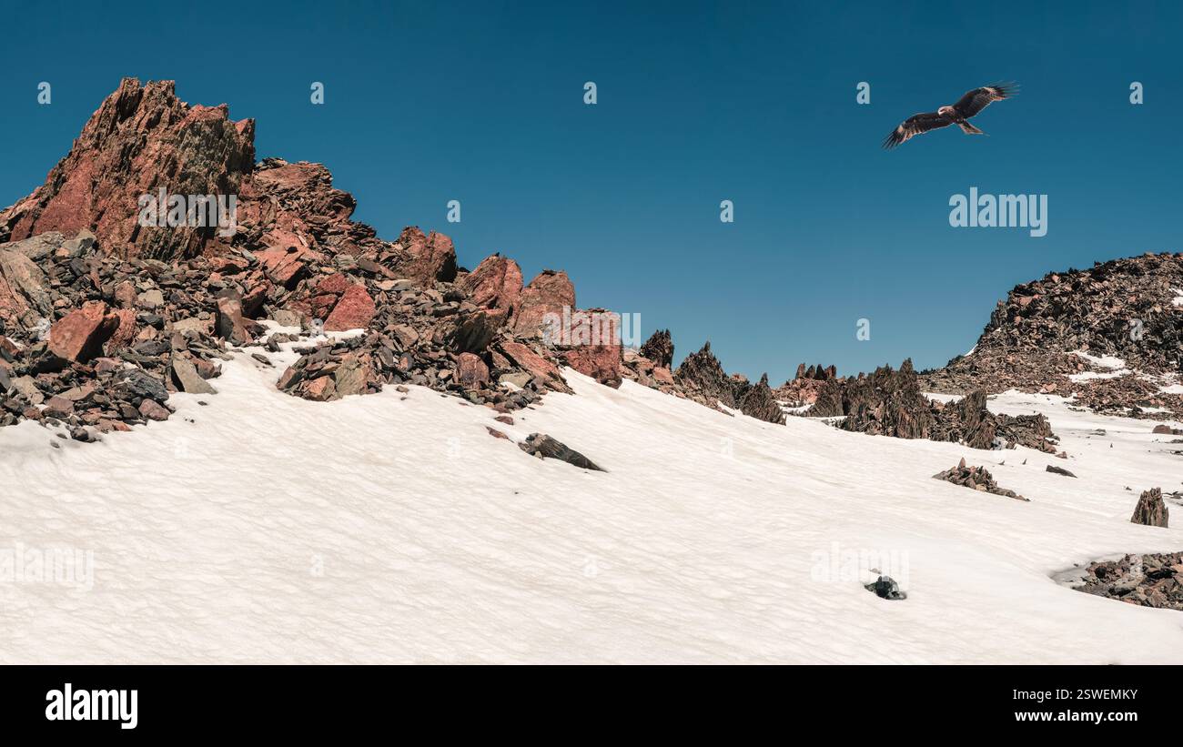 Panoramablick auf die scharfen Felsen, die von Schnee und Eis bedeckt sind. Ein Drachen fliegt über den Berg. Winter Berglandschaft. Stockfoto