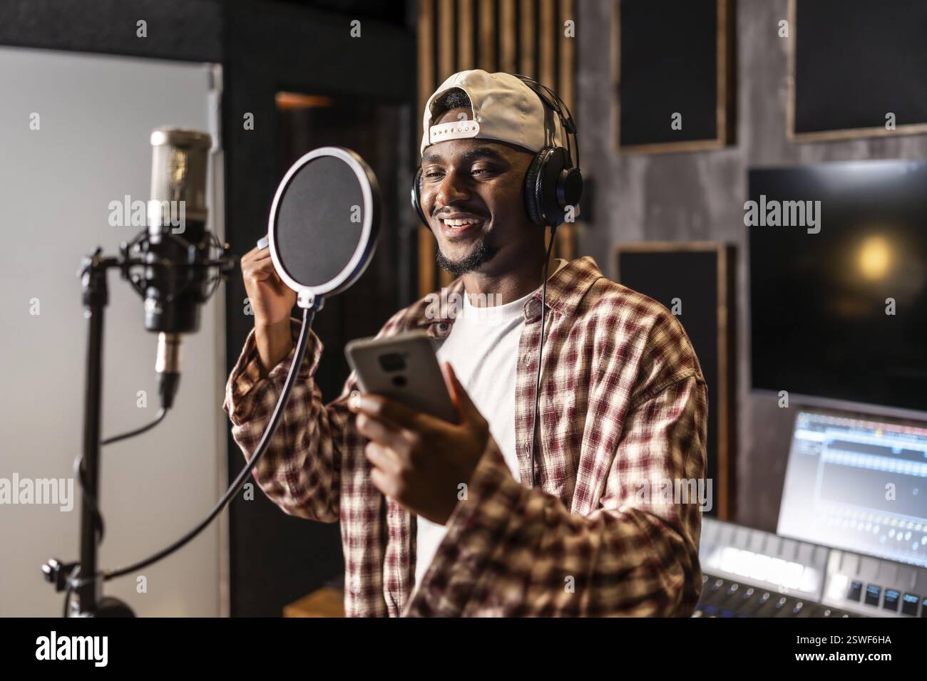 Junger, glücklicher, lächelnder Künstler, der im professionellen Studio Gesang für einen neuen Hit oder ein neues Album aufnimmt Stockfoto Junger, glücklicher, lächelnder Künstler, der im professionellen Studio Gesang für einen neuen Hit oder ein neues Album aufnimmt Stockfoto
