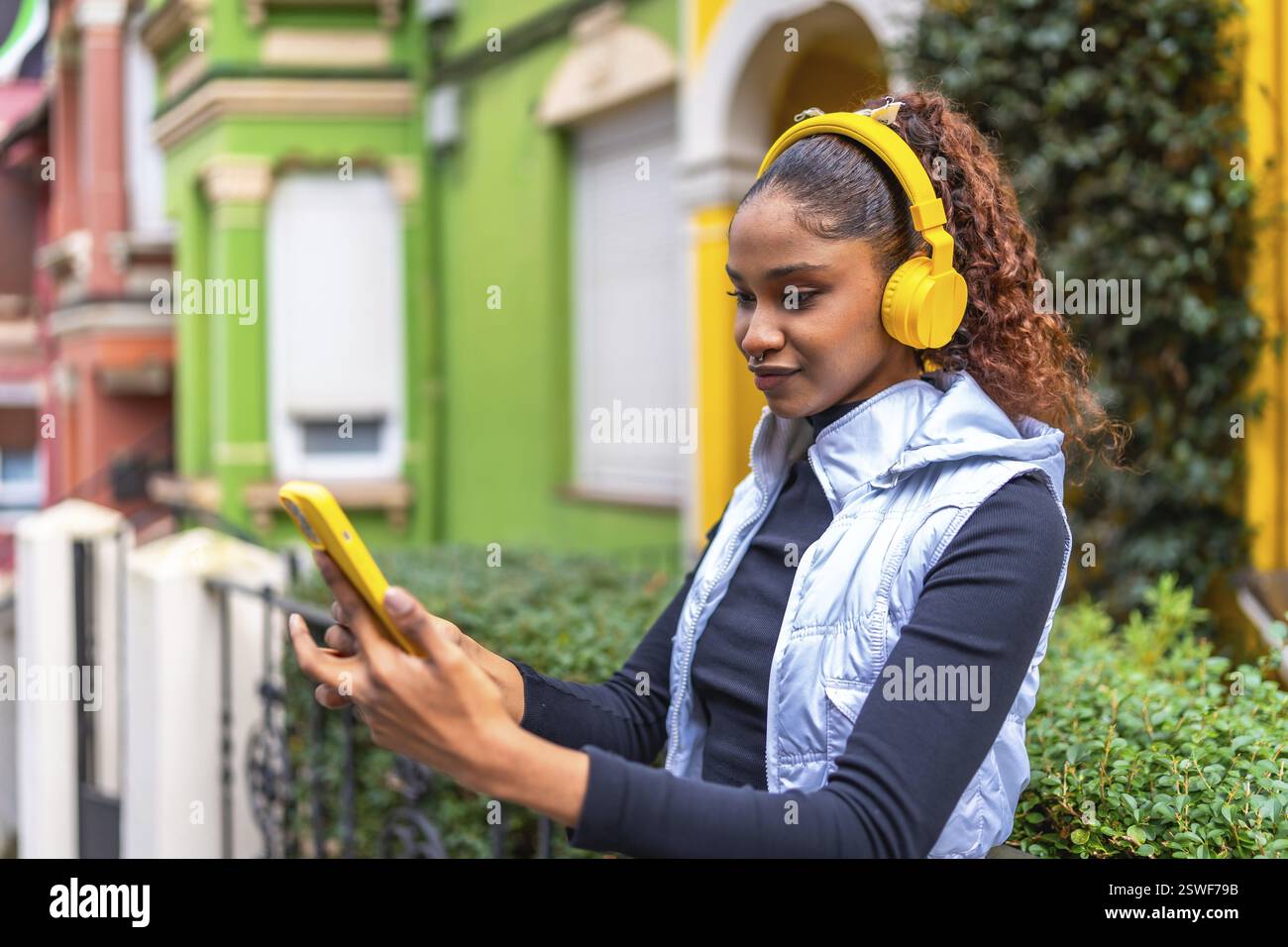 afroamerikanerin, die das Telefon benutzt, während sie Musik hört, die in einer bunten Straße steht Stockfoto