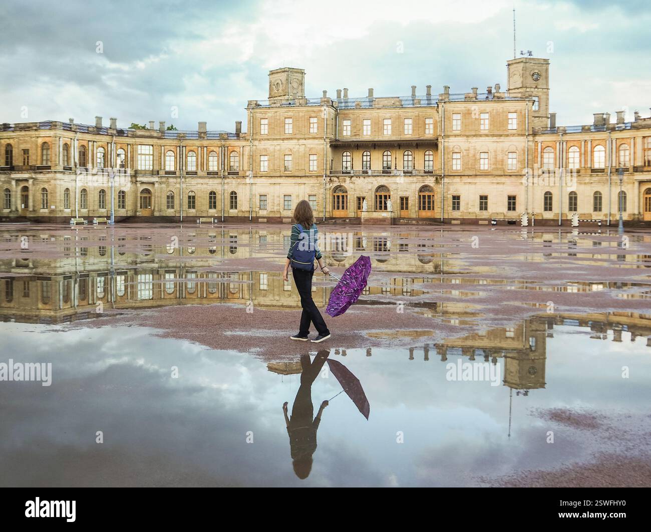 Eine Frau mit Rucksack und Schirm an einem wunderschönen historischen Ort vor dem Hintergrund eines alten Palastes. Gatchina Stockfoto