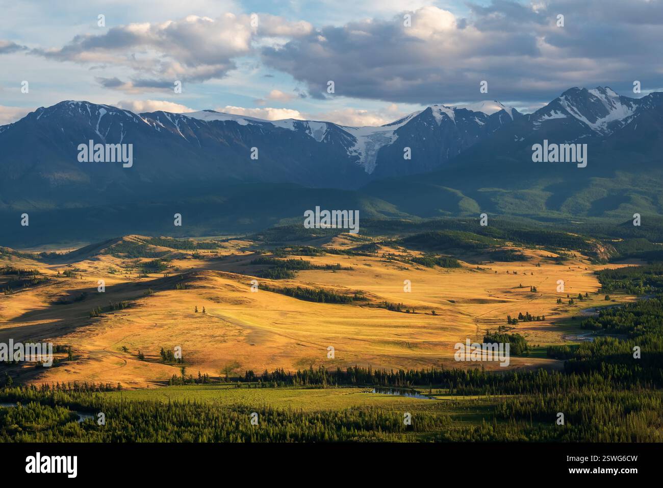 Malerischer, sonniger Blick auf das Waldtal mit Serpentinfluss gegen hoch verschneite Bergkette im Sonnenlicht. Wunderschöner Schlangenberg Stockfoto