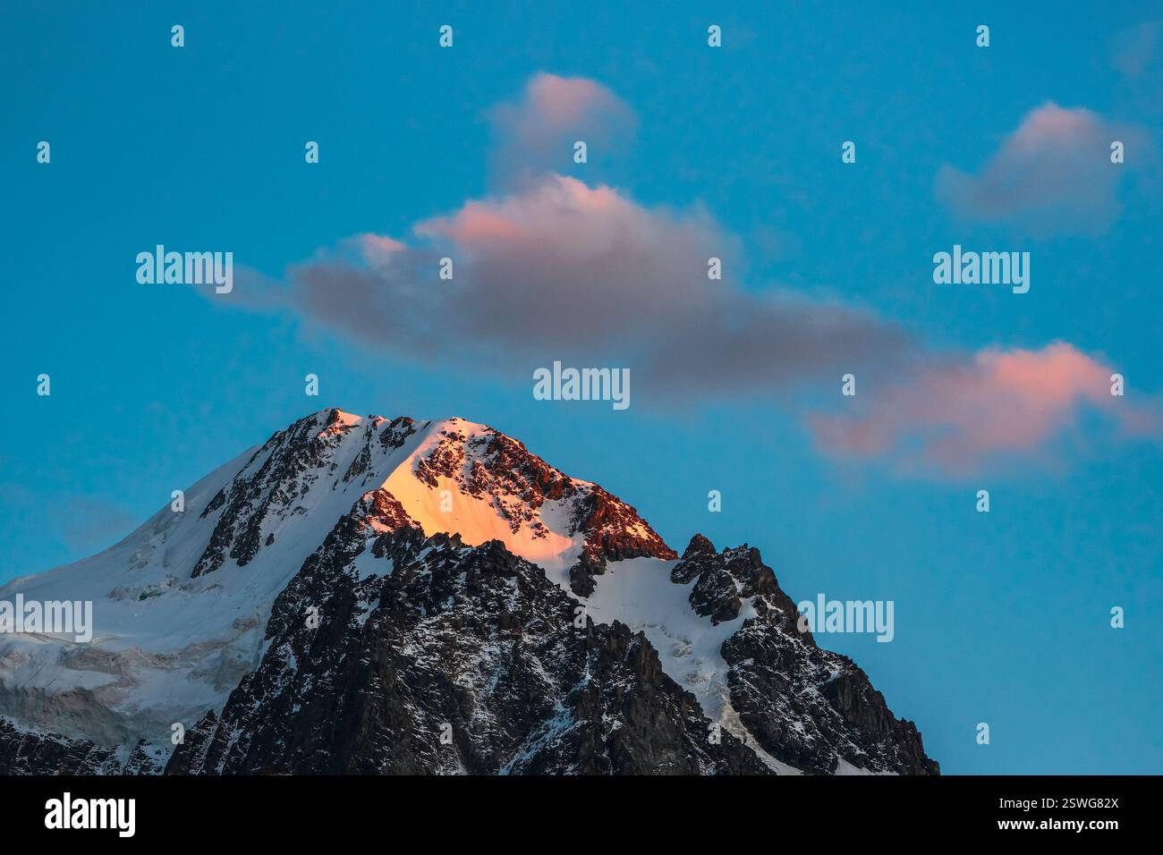 Oben schwarze Felsen im goldenen Sonnenschein am Abend und weißschneebedeckten spitzen Gipfel. Stimmungsvolle Dämmerungslandschaft mit hohen, schneebedeckten Bergen Stockfoto