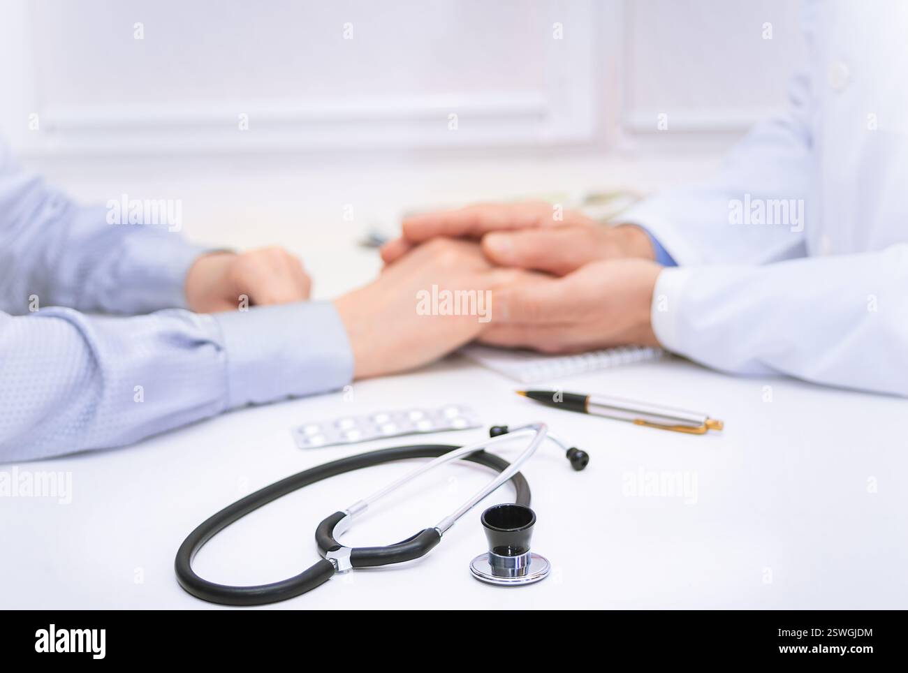 Ein Arzt beruhigt den Patienten durch unterstützende Berührung in einer klinischen Umgebung, während er Behandlungsoptionen und gesundheitliche Bedenken diskutiert. Stockfoto