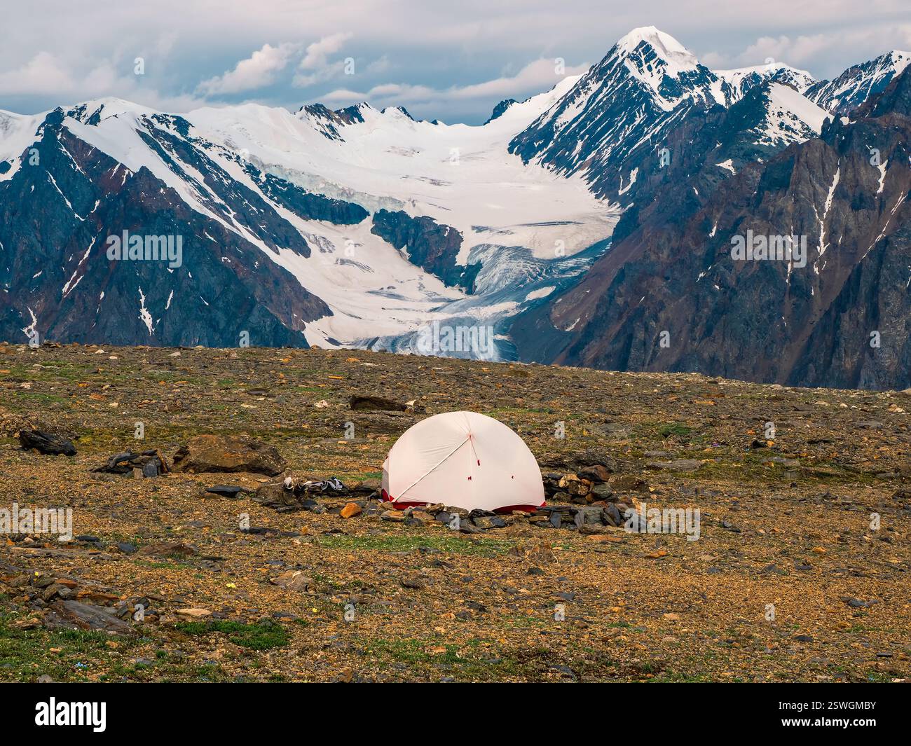 Trekking für Alleinreisende. Camping auf einem felsigen Hochplateau. Weißes Zelt vor dem Hintergrund des Gletschers und der hohen schneebedeckten Berge. Stockfoto