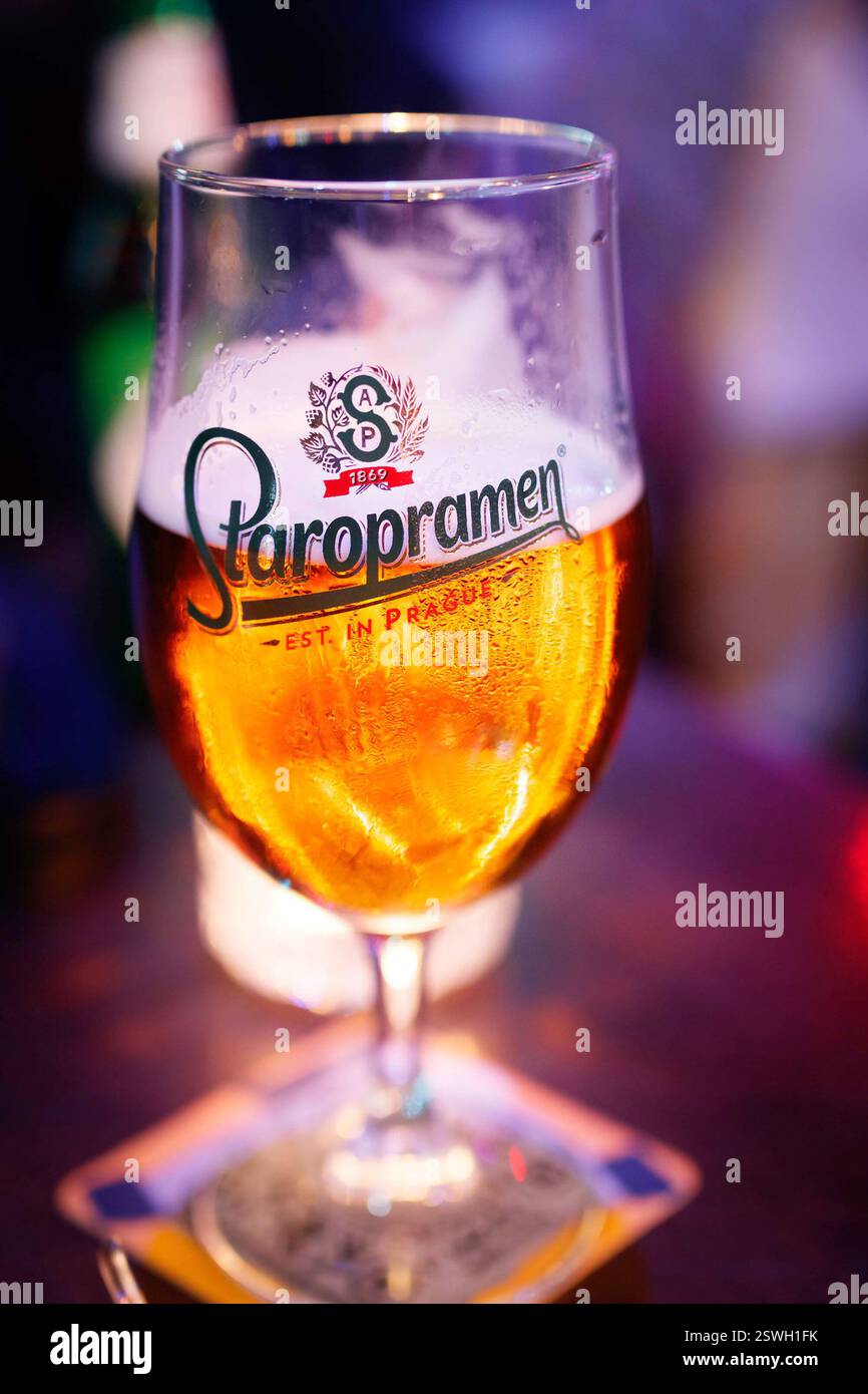 Ein Glas Staropramen-Bier auf einer Achterbahn in einer schwach beleuchteten Bar mit farbenfroher Beleuchtung und verschwommenem Pub-Hintergrund Stockfoto